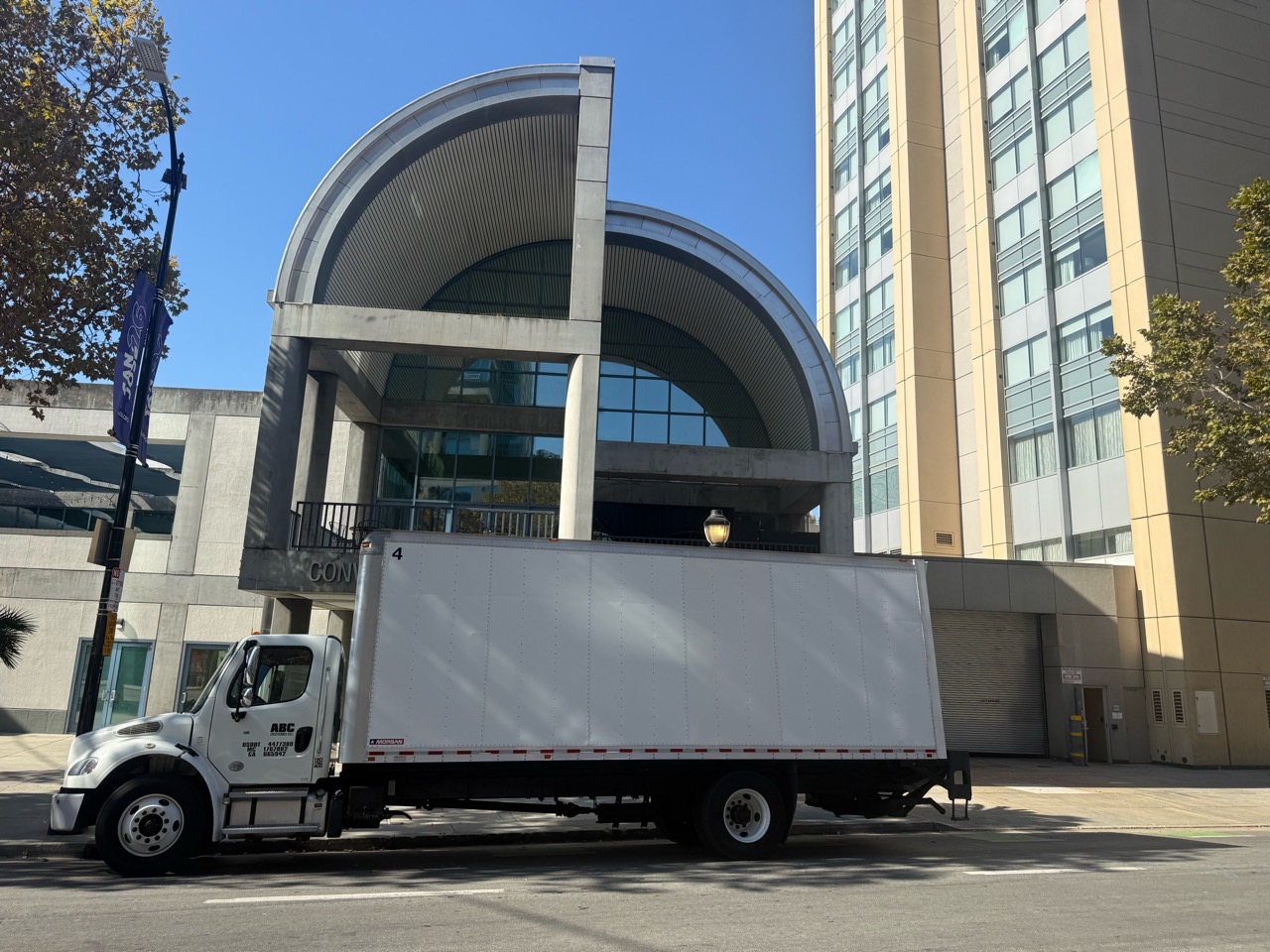 Full side profile of ABC DELIVERED's white 26-ft box truck in front of a commercial building